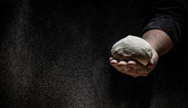 Pizza hamuru, erkek elleri un ile hamur yapıyor. Dondurucu bir hareketle siyah üzerine siyah bir un bulutu, kopyalama alanı, uzun afiş formatı.,