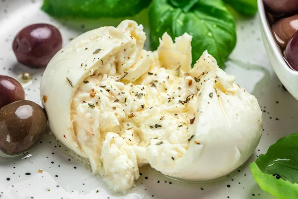 Beyaz tabakta fesleğenli ve zeytinyağlı kremalı İtalyan Burrata peyniri. İtalyan Akdeniz mutfağı. Yemek tarifi geçmişi. Kapat..