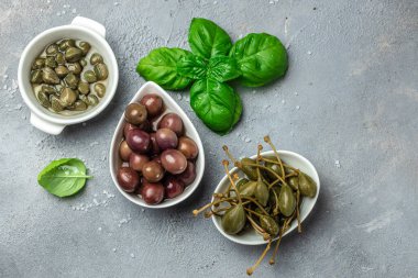 Gri arka planda taze fesleğen yapraklarıyla beyaz tabakta kapari üzümü ve zeytin. Akdeniz atıştırmalıkları. afiş, menü, metin için tarif yeri, üst görünüm,