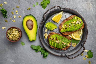 Kahvaltıda sağlıklı avokado tostları ya da öğle yemeğinde çavdar ekmeği, dilimlenmiş avokado, balkabağı tohumu, tuz ve biber. Vejetaryen yemeği. Bitki temelli diyet. Temiz yemek. Üst Manzara. Boşluğu kopyala,