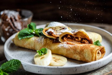 Çikolata kaplı krepler ve beyaz tabakta muz. İnce krep, blini. Lezzetli kahvaltı ya da atıştırmalık. Yemek tarifi geçmişi. Kapat..