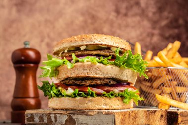 Ev yapımı XXL burger sığır eti, sebze, patates kızartması ve ahşap arka planda. Fast food ve abur cubur kavramı.