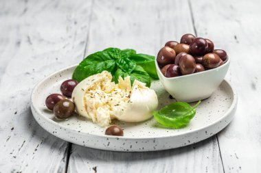 Beyaz tabakta fesleğenli ve zeytinyağlı kremalı İtalyan Burrata peyniri. İtalyan Akdeniz mutfağı. Yemek tarifi geçmişi. Kapat..
