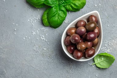 Zeytin. Taze fesleğen yapraklarıyla marine edilmiş ya da salamura edilmiş gri arka planda küçük bir kasede. afiş, menü, metin için tarif yeri, üst görünüm.