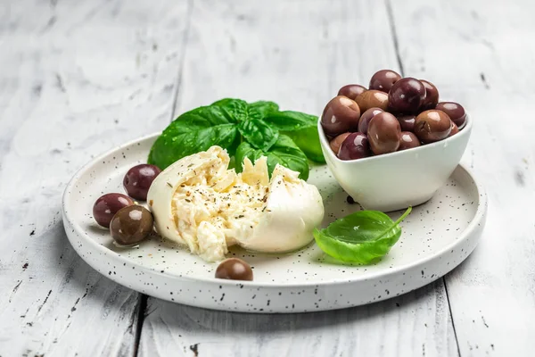 Beyaz tabakta fesleğenli ve zeytinyağlı kremalı İtalyan Burrata peyniri. İtalyan Akdeniz mutfağı. Yemek tarifi geçmişi. Kapat..