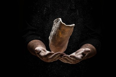 Un dağılmış halde pizza hamuru uçurmak. Siyah üzerine bir un bulutunun dondurucu hareketiyle. Hamur yoğuran elleri pişir. Boşluğu kopyala.