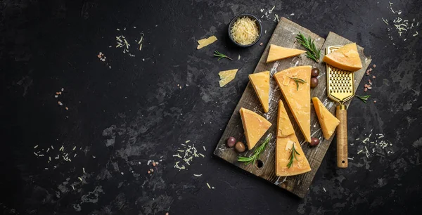 Tahtada parmesan peyniri, sert peynir, zeytin, biberiye ve siyah arka planda metal rendesi. Uzun afiş biçimi. en üstteki görünüm.