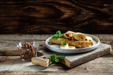 Çikolata kaplı krepler ve beyaz tabakta muz. İnce krep, blini. Lezzetli kahvaltı ya da atıştırmalık. Yemek tarifi geçmişi. Kapat..