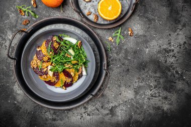 Arugula, pancar ve portakal salatası, çatallı ceviz, sos ve gri arka planda baharat, vitamin salatası. Düzgün beslenme. metin için yer, üst görünüm.