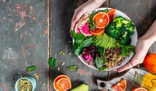 Kızların elleri Quinoa sebzeli vejetaryen Buda kâsesi avokado, kan portakalı, brokoli, karpuz turpu, ıspanak, kinoa, balkabağı çekirdeği. en üstteki görünüm.