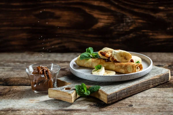 Çikolata kaplı krepler ve beyaz tabakta muz. İnce krep, blini. Lezzetli kahvaltı ya da atıştırmalık. Yemek tarifi geçmişi. Kapat..