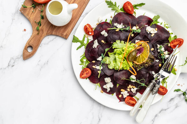 Beet or beetroot salad with greens, cheese, nuts, cranberries on plate with fork, dressing and spices on white background. italian cuisine. banner, menu, recipe place for text, top view,