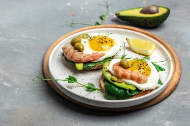 Açık sandiviçli tam yağda yumurta, ıspanak, avokado, gri arka planda karides, ketogenik kahvaltı. Süper yiyecek konsepti. Sağlıklı, temiz yemek. Üst görünüm.