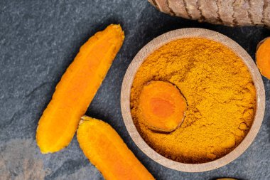 Zerdeçal köklü kaşık içinde zerdeçal tozu. Beton arka planda sokağa çıkma yasağı veya kömür tabakası. Baharat, doğal renklendirme, alternatif tıp. en üstteki görünüm.