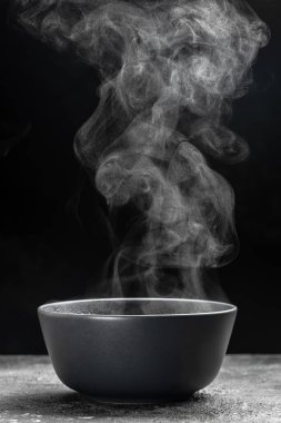 Bir kase sıcak dumanlı çorba. Koyu arkaplanda siyah seramik kase. Sıcak yemek. Aşçılık, aşçılık, konsept.