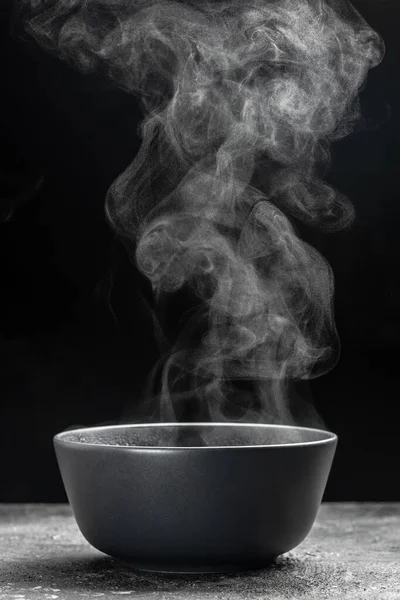 Bir kase sıcak dumanlı çorba. Koyu arkaplanda siyah seramik kase. Sıcak yemek. Aşçılık, aşçılık, konsept.