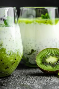 Sağlıklı kahvaltı pudingi, beyaz bir masada cam kavanozlarda kivi var. Temiz yemek, diyet, vejetaryen yemek konsepti. dikey resim.