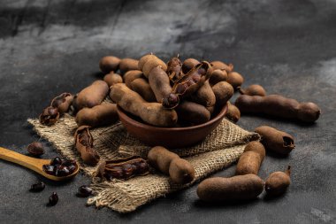 Tropikal meyveler, kahverengi bir kasapta kabuklu Tamarindo fasulyeleri koyu bir arka planda, sağlıklı meyveler. afiş, menü, metin için tarif yeri, üst görünüm.