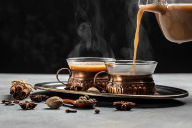 Hint masala çayı. Süt ve baharatlı sıcak masala çayı koyu arkaplanda cam bir bardağa dökülür. Uzun afiş biçimi. metin için yer.