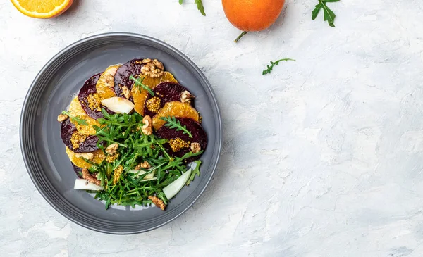 Arugula, pancar ve portakal salatası, çatallı ceviz, sos ve gri arka planda baharat, vitamin salatası. Düzgün beslenme. metin için yer, üst görünüm.