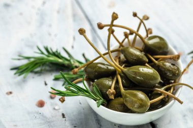 Kapari. Salamura edilmiş ya da turşulu kapari meyvesi. Küçük bir kasede taze biberiye, gri arka planda. metin için yer, üst görünüm.