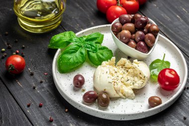 Kremalı İtalyan Burrata peyniri fesleğenli, zeytinyağlı ve beyaz tabakta vişneli domatesli koyu ahşap arka planda. afiş, menü, metin için tarif yeri, üst görünüm.