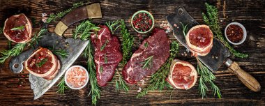 Çiğ et fileto Mignon bifteği üzerine biber ve tuz, fileminyon. Domuz pastırmasına sarılı sığır filetosu biftekleri ve koyu arkaplanda kekik. Uzun afiş biçimi. en üstteki görünüm.