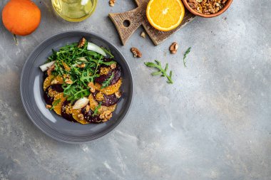 Arugula, pancar ve portakal salatası, çatallı ceviz, sos ve gri arka planda baharat, vitamin salatası. Düzgün beslenme. metin için yer, üst görünüm.