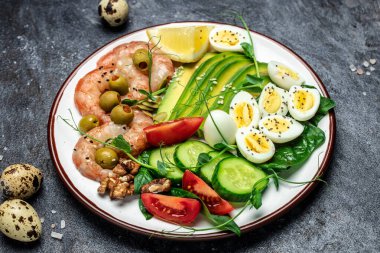 Ketojenik kahvaltı. Düşük karbonhidratlı karides, karides, bıldırcın yumurtası, taze salata, domates, salatalık ve avokado. Keto diyeti. Üst görünüm.