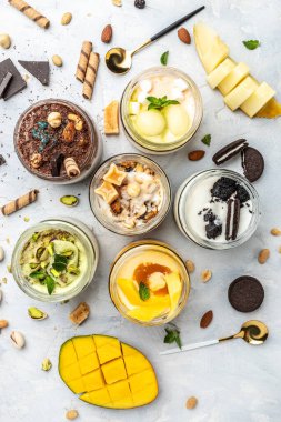 Cam kavanozda servis edilen lezzetli dondurma, İtalyan tatlı dondurması şam fıstığı, çikolata, karamel, kavun, mango, çikolatalı sandviç kurabiyeleri, dikey görüntü. en üstteki görünüm,