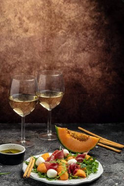 Akdeniz salatası jambon, mozzarella ve yeşil fesleğen yaprakları ve kavun kavunu beyaz masada, geleneksel İspanyol ve İtalyan aperatifi toptan Grissini ile servis edilir..