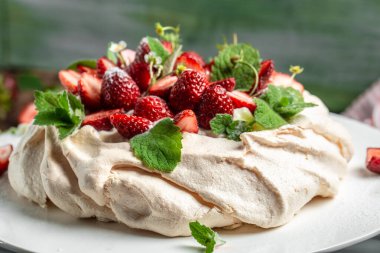Ev yapımı lezzetli kremalı Pavlova kremalı, taze çilekli ve ahşap arka planda naneli, yazı için yer, üst manzara..