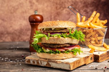 Ev yapımı XXL burger sığır eti, sebze, patates kızartması ve ahşap arka planda. Fast food ve abur cubur kavramı.