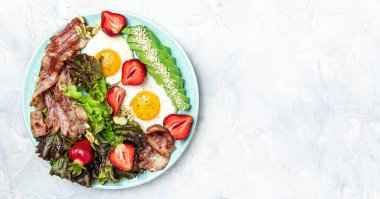 Ketojenik diyet yiyecekler, avokadolu kızarmış yumurta pastırması, çilek ve hafif arkaplanda taze salata. Sağlıklı yemek konsepti, uzun afiş formatı. en üstteki görünüm.