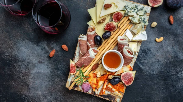Appetizers table with italian antipasti snacks and wine in glasses. cheese, ham, nuts, fruit, bread sticks. Delicious balanced food concept, top view.