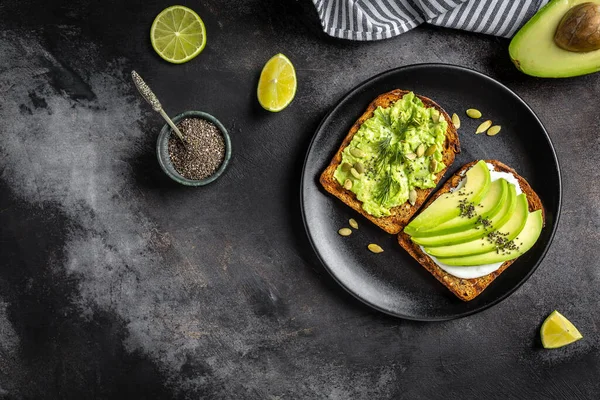 Kahvaltı veya çavdar ekmeği, avokado, roka, kabak ve susam, tuz ve biber dilimlenmiş ile öğle yemeği için sağlıklı avokado kızartır. Vejetaryen yiyecekler. Bitki temelli diyet. Temiz yemek. Üstten görünüm. Kopya alanı