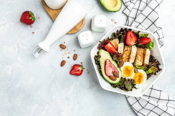 Ketogenic low carbs diet. Plate with keto foods: two eggs, avocado, grilled chicken fillet, nuts, strawberries and fresh salad. Healthy fats, clean eating for weight loss. view.