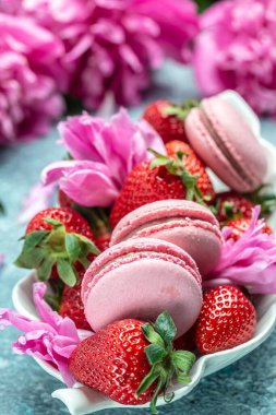 Pembe şakayık çiçeği ve makarna kurabiyeleri ve mavi arka planda tatlı çilek. Meyveli küçük Fransız pastaları. en üstteki görünüm.