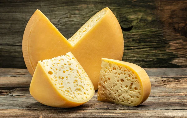 奶酪轮与切块奶酪三角形形状从一个巨大的奶酪头 木制底座上有大孔的奶酪玛斯坦 — 图库照片
