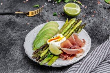 kuşkonmaz, avokado, haşlanmış yumurta, jambon, pastırma. Siyah arka planda. Keto Paleo öğle yemeği Üst Manzara