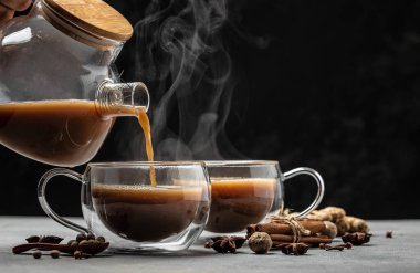 Hint masala çayı. Süt ve baharatlı sıcak masala çayı koyu arkaplanda cam bir bardağa dökülür. Uzun afiş biçimi. metin için yer.