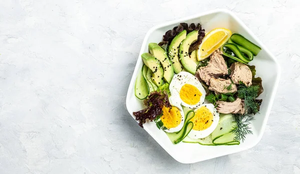 Ketogenic low carbs diet, Plate with keto foods: two eggs, avocado, tuna, cucumber and fresh salad. Healthy fats, clean eating for weight loss. top view.