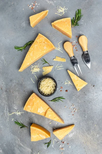 Parmesan cheese on a wooden board, Hard cheese, rosemary and cheese knife on a gay background. vertical image. top view.
