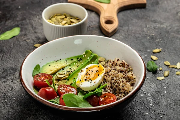 Keto diet plate quinoa, avocado, egg, tomatoes, spinach and sunflower seeds on dark background. Healthy food, ketogenic diet, diet lunch concept, place for text, top view.
