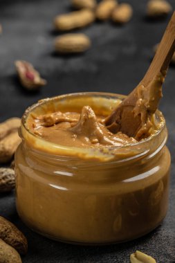 Cam kavanozda fıstık ezmesi ve gri arka planda kaşık, Amerikan tatlı konsepti. dikey görüntü. Üst Manzara. metin için yer.