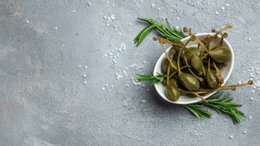 Kapari. Salamura edilmiş ya da turşulu kapari meyvesi. Küçük bir kasede taze biberiye, gri arka planda. metin için yer, üst görünüm.