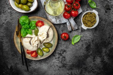 İtalyan domatesleri ve burrata peynirli salata yanında vişneli domates, taze fesleğen yaprağı, jambon ve koyu arkaplanda zeytin. Restoran menüsü üst görünümü.