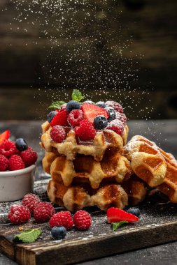 Sweet Homemade Berry Belgian Waffle with with raspberries, strawberries and blueberries, sugar powder in a freeze motion of a cloud of powder midair.