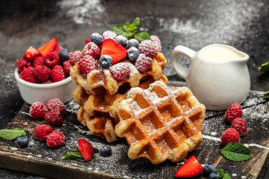 Ahududu, çilek ve yaban mersinli Belçika waffleları, siyah arkaplanda şeker tozu.