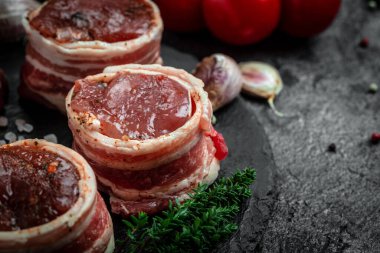 Çiğ et fileto mignon bifteği, metel tepside, biber ve tuzlu, fileminyon. Domuz pastırmasına sarılı sığır filetosu biftekleri ve koyu arkaplanda kekik. en üstteki görünüm.